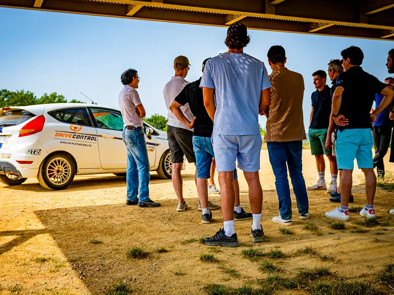 Groupe de participants réunis autour d’une voiture de rallye pour le briefing