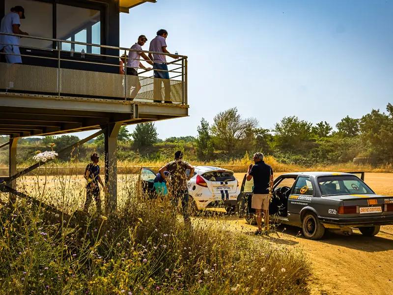 Groupe de participants sur la terrasse de la tour de contrôle du circuit, deux voitures de rallye en contrebas